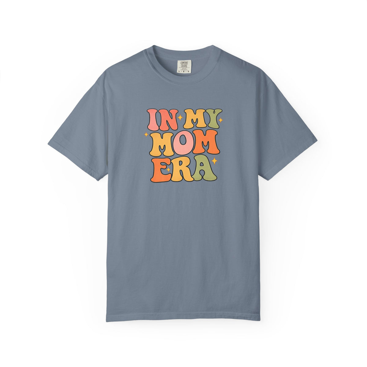 A slate blue short-sleeve t-shirt with a retro-style multicolor graphic on the chest that reads 'IN MY MOM ERA' in wavy, bubble letters.