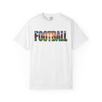 A white short-sleeve crewneck t-shirt featuring the word 'FOOTBALL' printed across the chest in a colorful landscape graphic containing green grass, blue sky, and orange sunset tones, displayed on a clean white background.