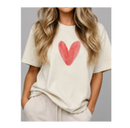 A woman wearing a cream-colored short-sleeve t-shirt with a red watercolor heart graphic on the chest, paired with light beige sweatpants, set against a solid gray background.