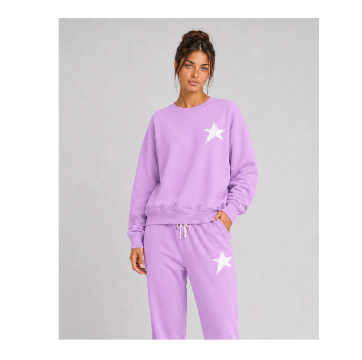 A woman modeling a matching lavender sweatshirt and jogger pants set with white star graphics on a light gray studio background.